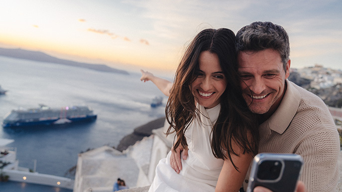 Couple taking a selfie overlooking the ocean and a cruise ship in Santorini at sunset