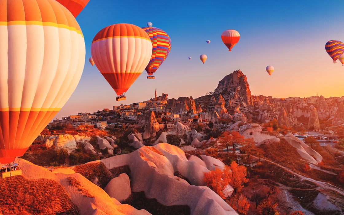 Colorful hot air balloons floating above unique rock formations during a vibrant sunset.