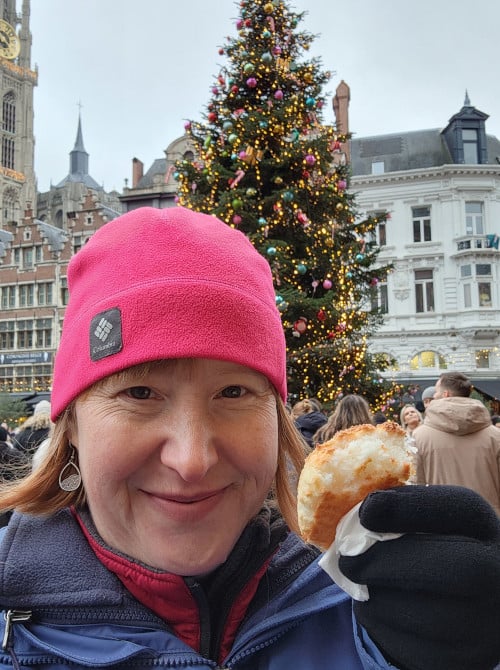 Provident Travel Advisor Michelle Boyles savoring a pastry in bustling European city square decorated with a Christmas tree