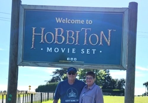Provident Travel Advisor Cindy Moore and her husband in front of Hobbiton sign in New Zealand