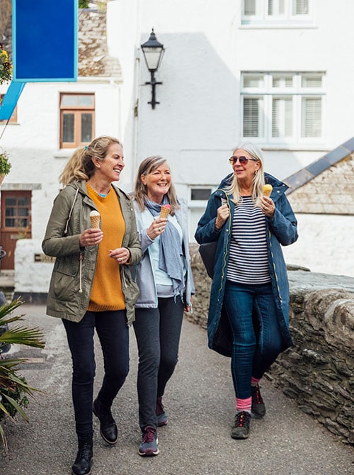 Three women enjoying ice cream while walking together through a charming European village.