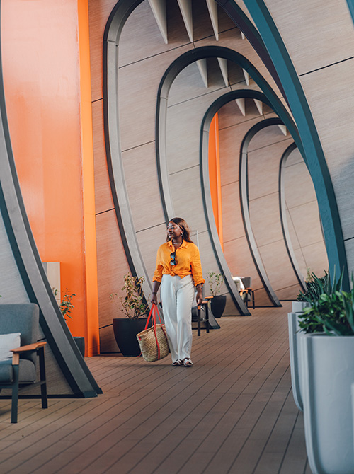 Woman in yellow shirt wheeling suitcase aboard Celebrity cruise ship resort deck