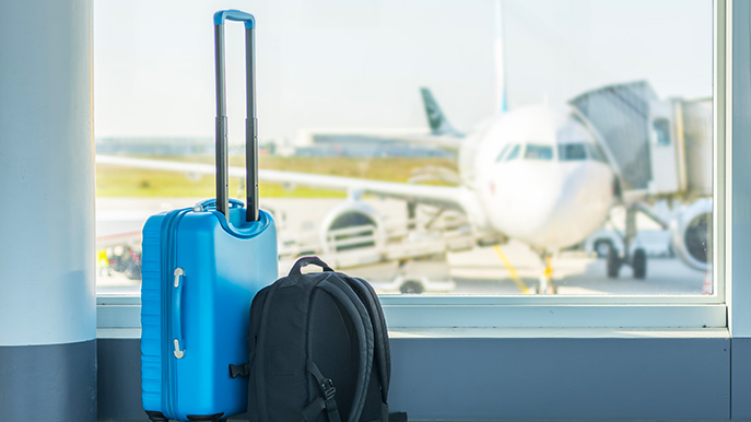Blue suitcase and black backpack near an airport window with an airplane in the background