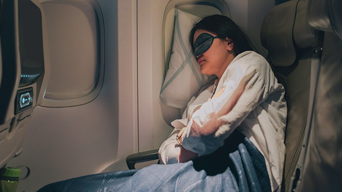 Person sleeping in an airplane seat by the window with an eye mask and a blue blanket