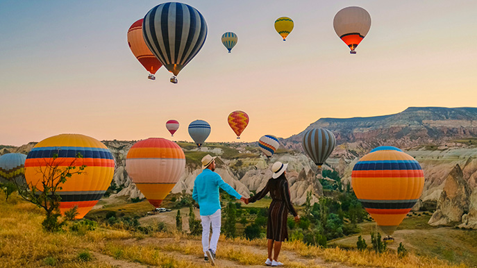 Couple watching hot air balloons over a rocky landscape at sunrise