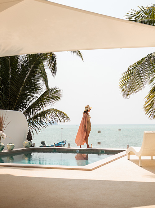 Woman walking by a pool with palm trees and ocean in the background