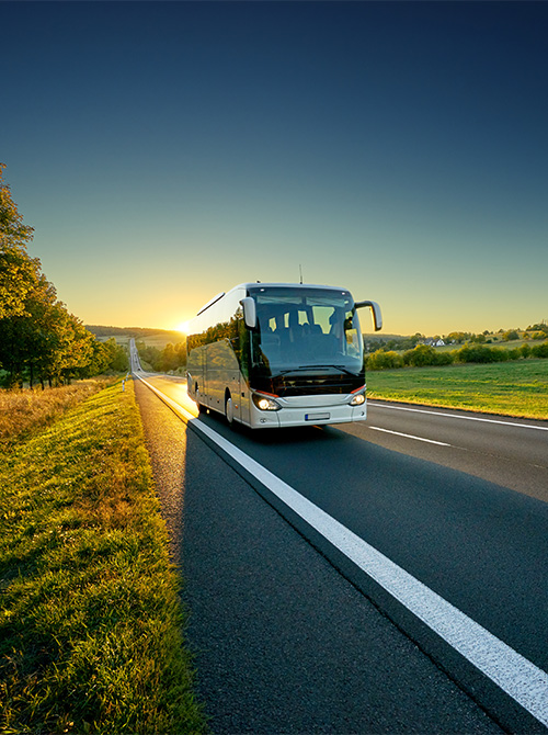 White motorcoach traveling on asphalt country road at sunset