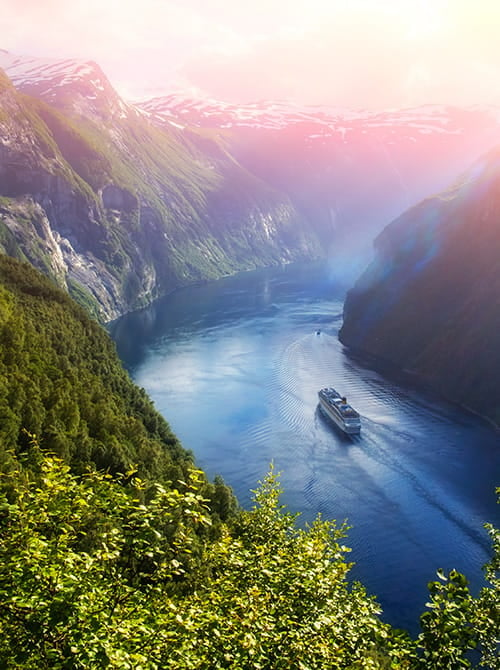 Cruise ship in the distance floating down a beautiful river surrounded by trees and mountains