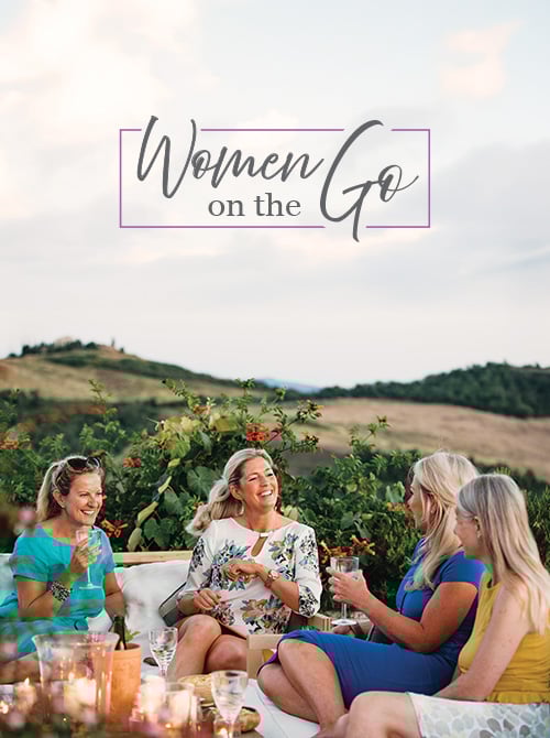 Women laughing and relaxing on vacation in Italy at sunset with Women on the Go logo in background