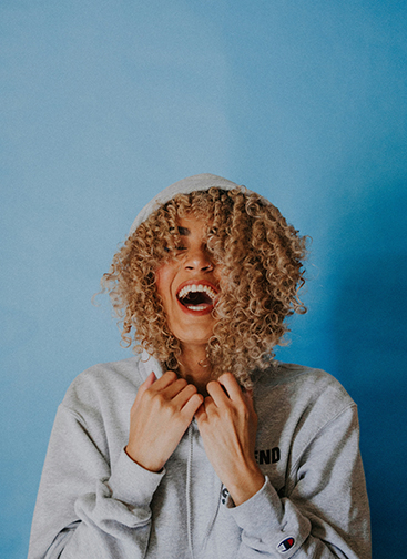 Woman wearing a hoodie and laughing in front of a bright blue backdrop