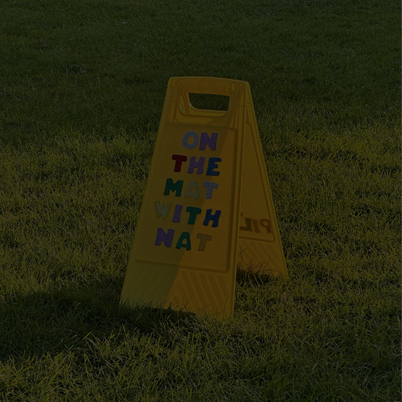 Yellow On the Mat with Nat sign on grass