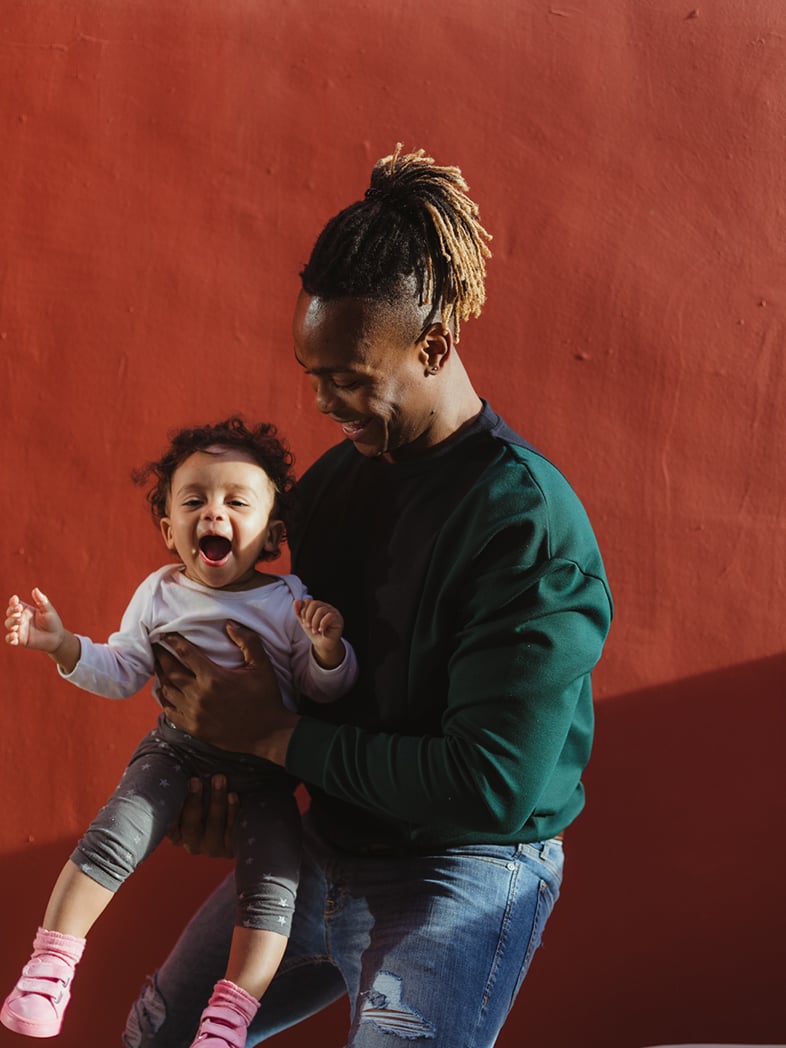 Man holding a laughing child in front of a red wall
