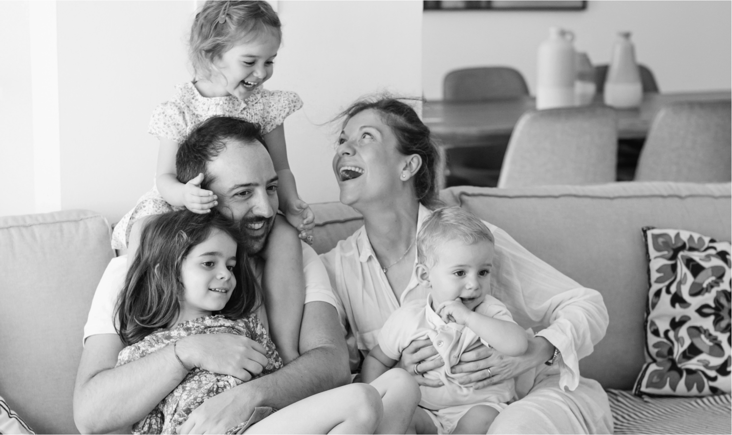 A family with three children sits on couch smiling.