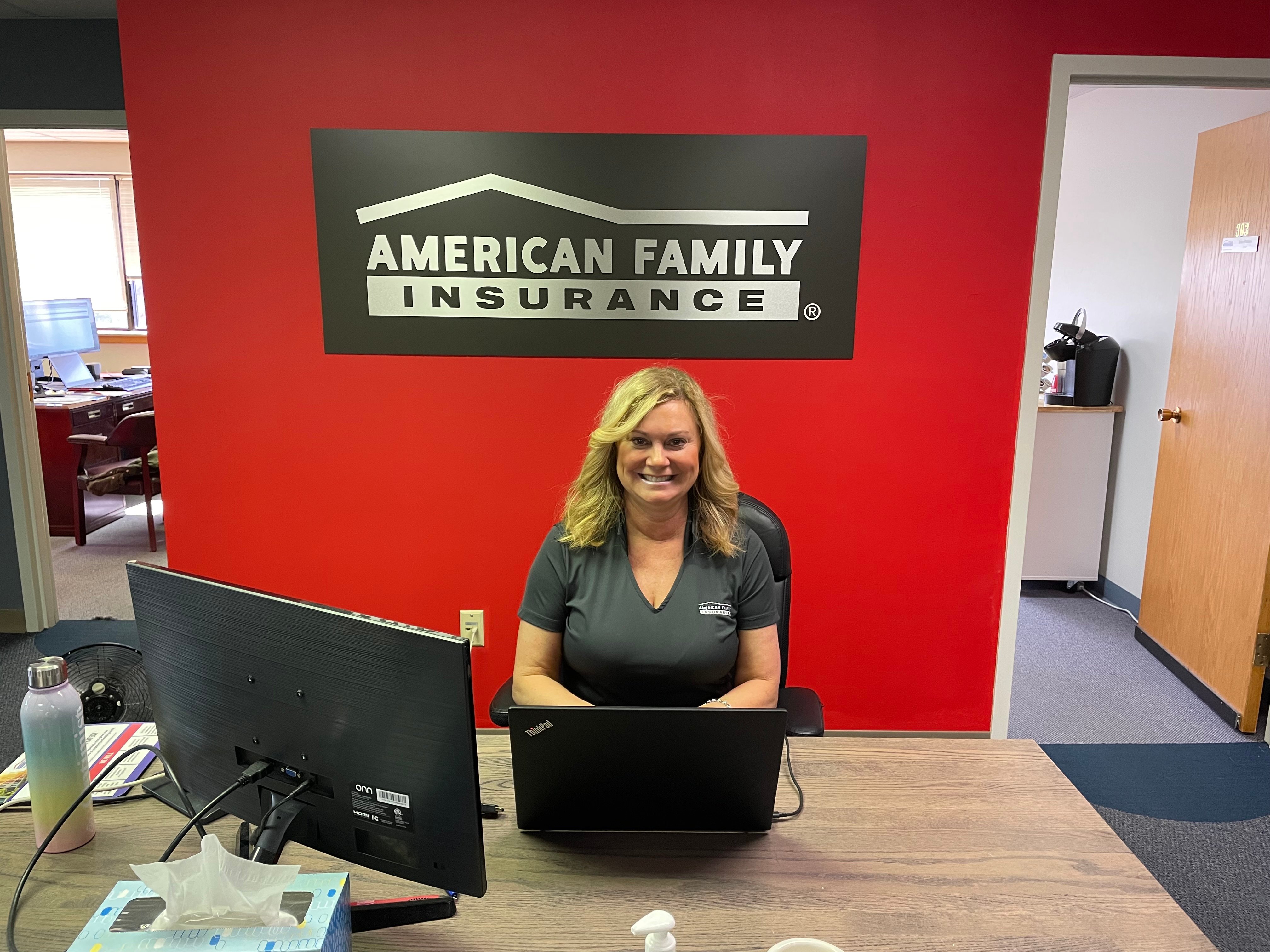 a woman sitting at a desk with a laptop and a sign behind her