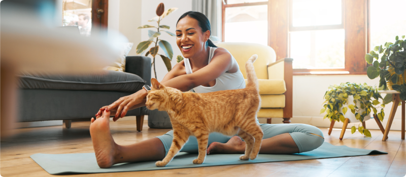 Woman doing Yoga on the floor with her pet cat walking by.