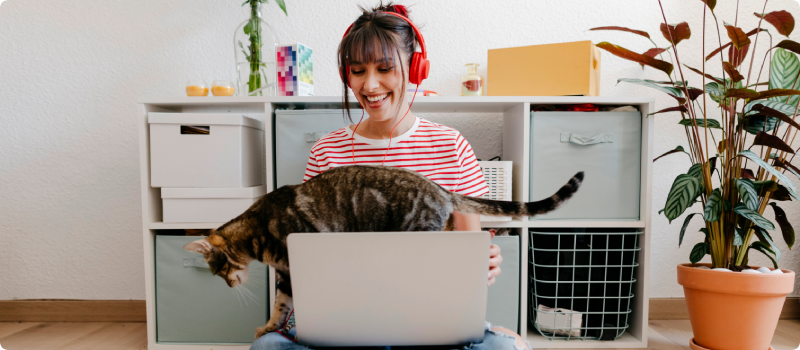 Young woman wearing headphones sitting with laptop and cat at home