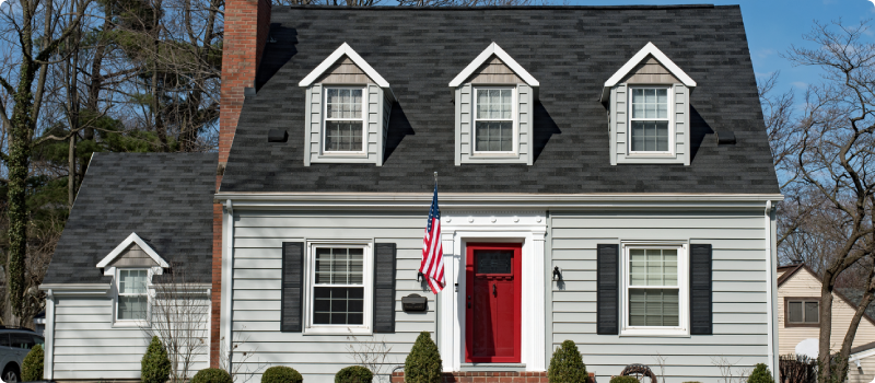 a gray Cape Cod style home with a red door