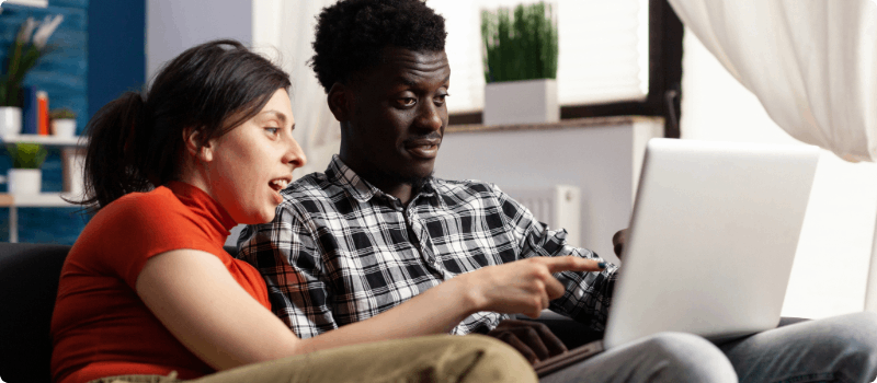Two people sitting on a couch and looking at a laptop.