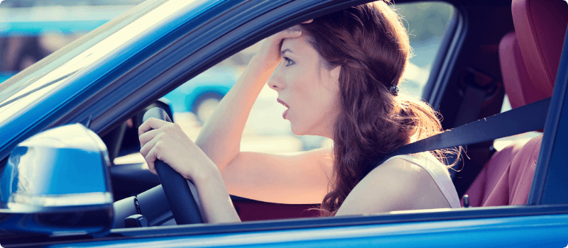 A shocked driver sitting behind the wheel with her hand on her forehead. 
