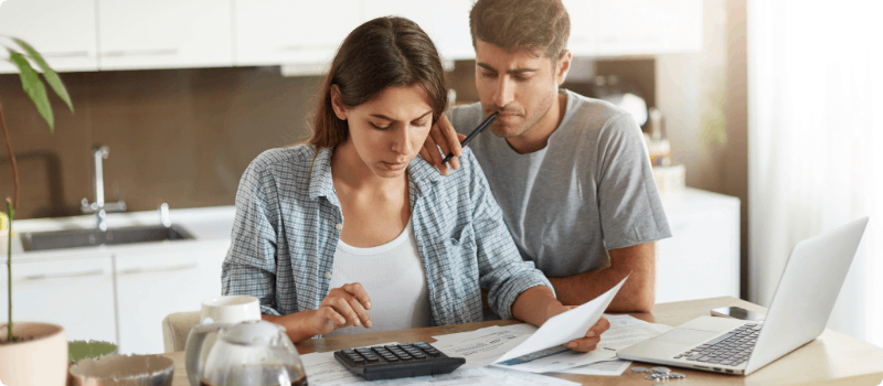 Two people sitting at a table while reviewing their bills with a calculator, documents and a laptop.