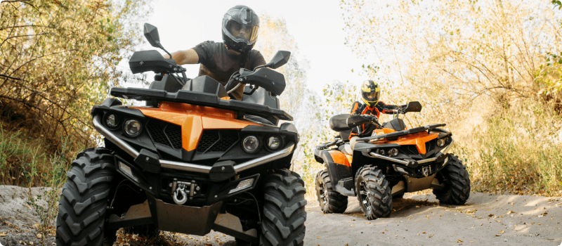 Two people riding ATVs on a dirt road.