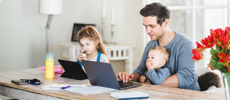 Father working from home at a large desk with his two small children.  