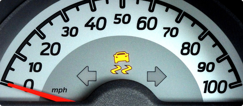A close-up of a car's dashboard featuring an illuminated yellow traction control light.