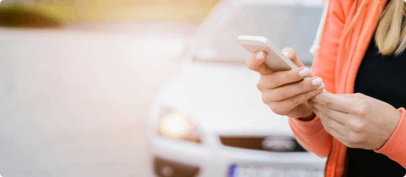 Person looking at her phone with her vehicle in the background.