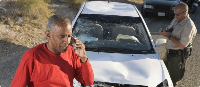 An accident victim on the phone as an officer writes a report.