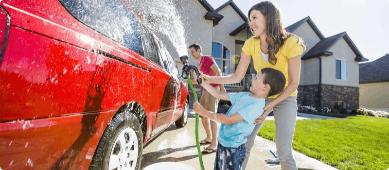 Happy mother and son washing car on sunny day. 