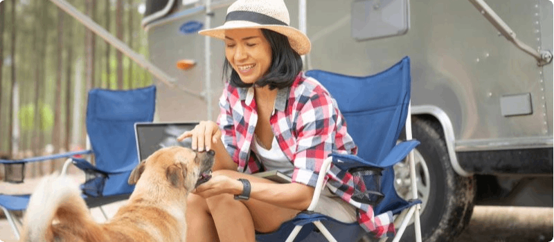 Happy woman sitting in front of her RV while petting her dog. 