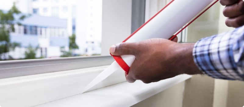 A close-up of a homeowner caulking their window.