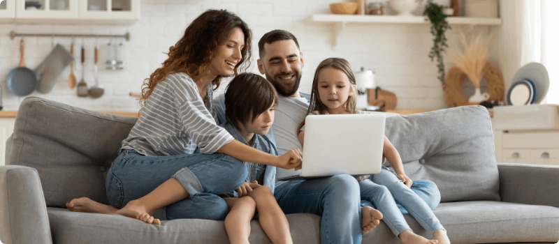 A happy family sitting on their living room couch with a laptop.