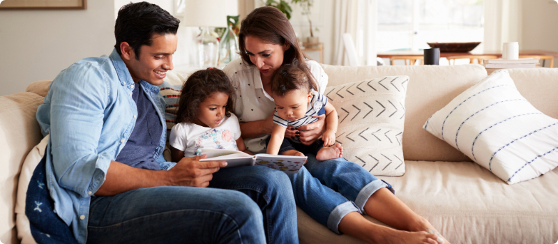 A family sitting on their couch and reading a book together.