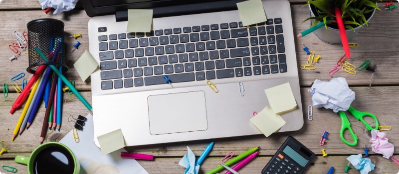 An old, worn laptop surrounded by a messy desk.