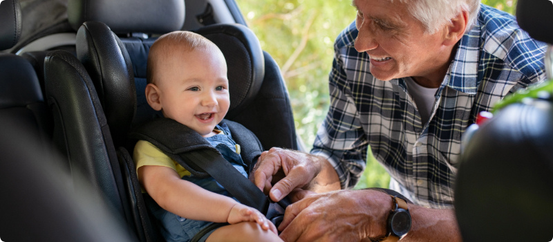 A grandfather placing his grandchild in a car seat. 