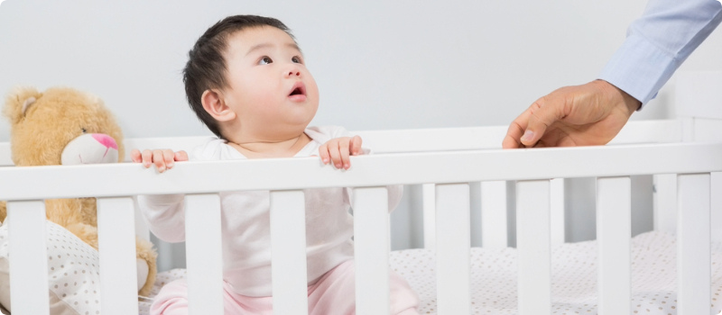 An infant in a crib, looking up at their parent.