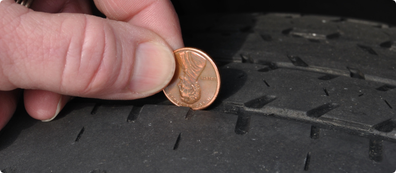 A person using a penny to check the tread on a tire.