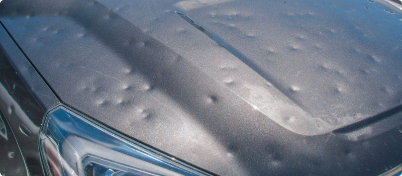 The hood of a vehicle presenting severe hail damage.