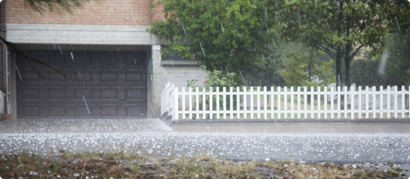 The front of a home's garage and fence amidst a hailstorm.