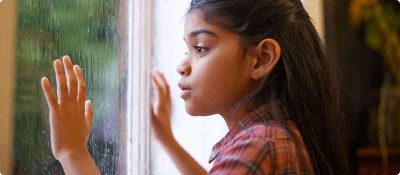 Young girl starting at a storm outside from a window. 