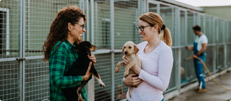 Two people holding puppies at an animal shelter.