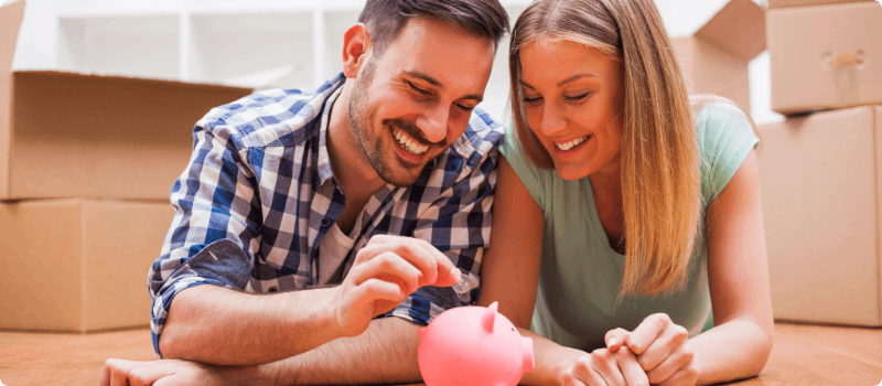 A happy couple placing a coin into a piggy bank.