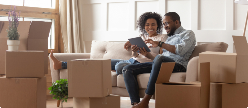 A happy couple sitting together on their couch, looking at their computer tablet.