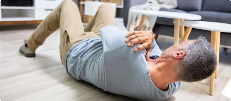 A person who has just fallen, lying on a living room floor while holding their shoulder.