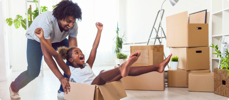 A happy parent, playing with their laughing child, pushing them across the floor in a box.