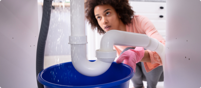 A concerned homeowner looking at a leaking pipe under her sink. 