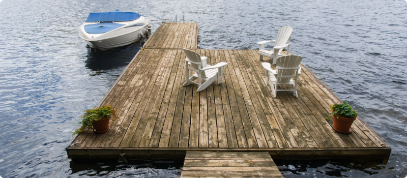 Three chairs on a home dock with a small boat anchored to it.