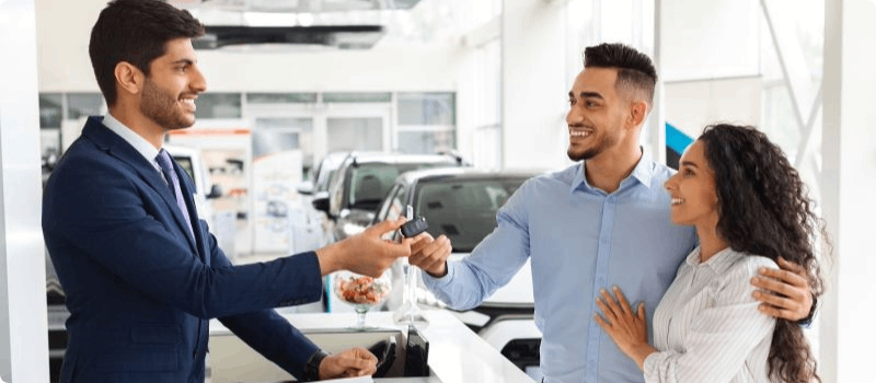 Auto salesperson handing car keys to a happy couple.  
