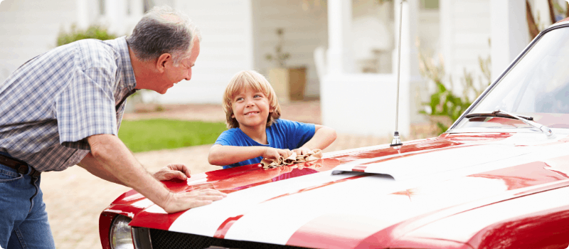 Grandfather washing his red sports car with his grandson. 